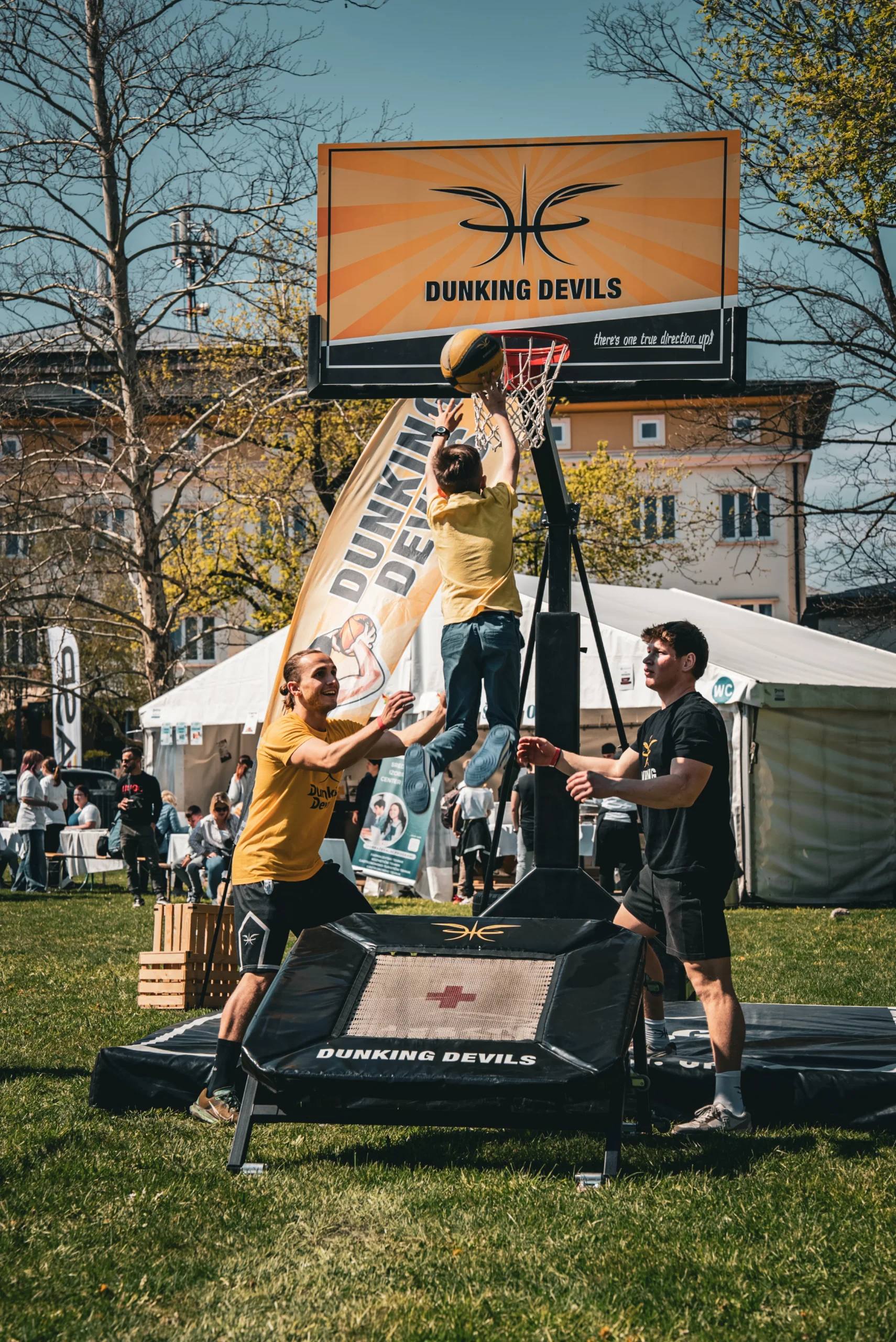 Dunking Devils dunk workshop outdoors: a young athlete dunks off a trampoline under the Dunking Devils hoop.