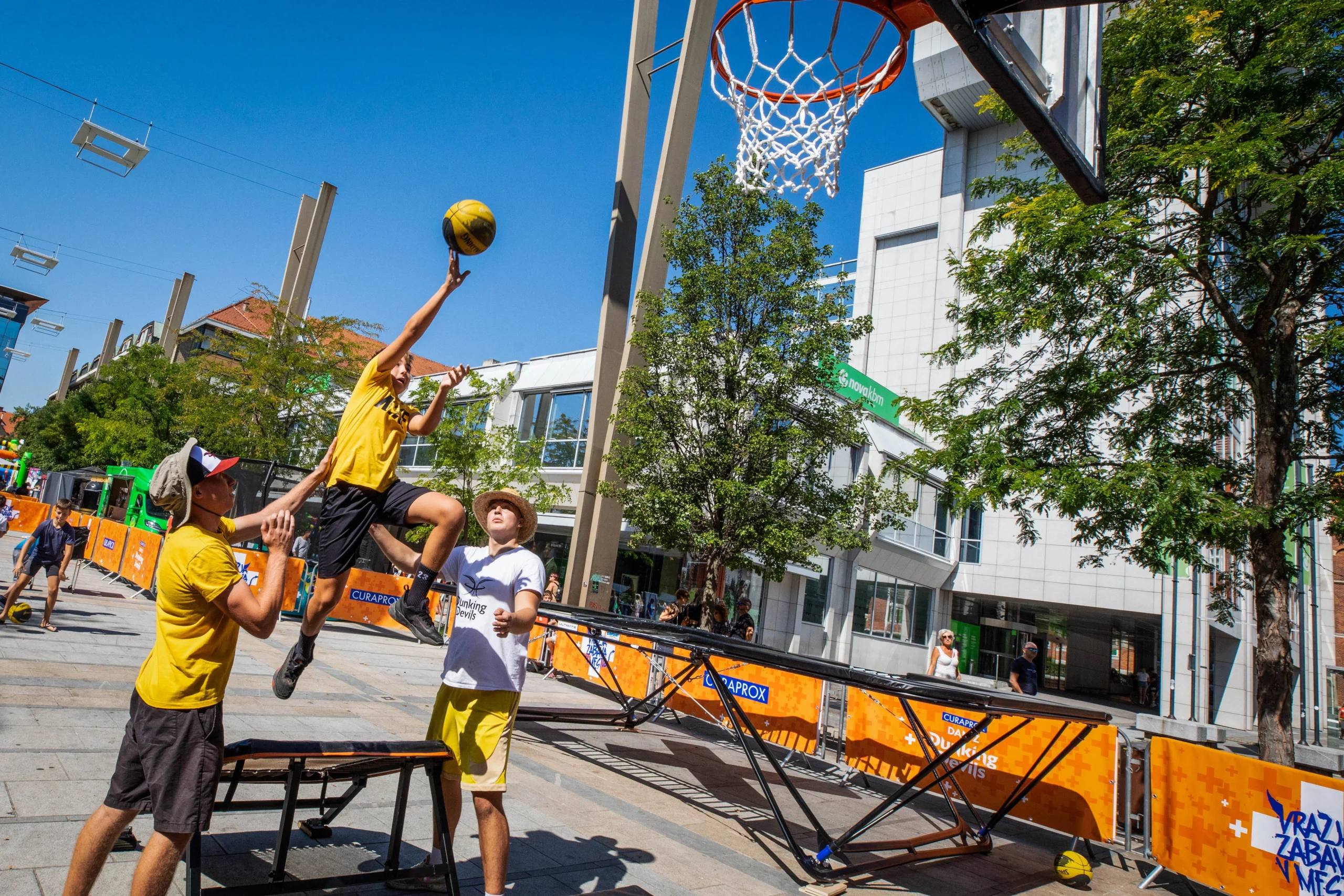 A boy jumps off a trampoline to dunk while a Dunking Devils coach spots him at an outdoor workshop.