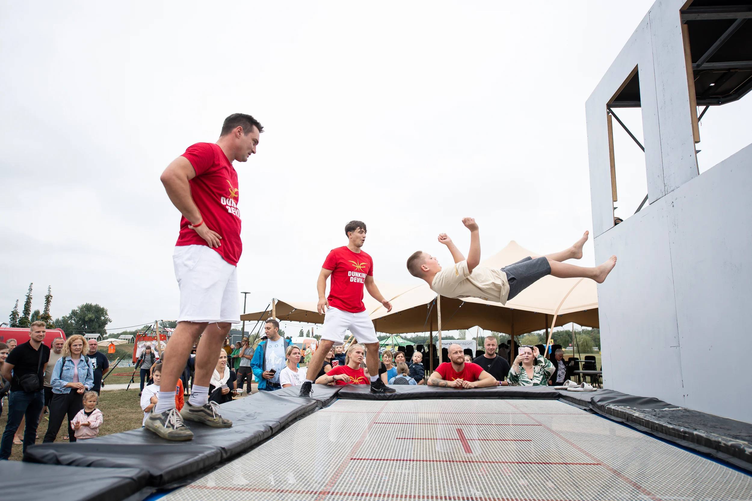 A teenager runs up the Dunking Devils trampoline wall while coaches watch.