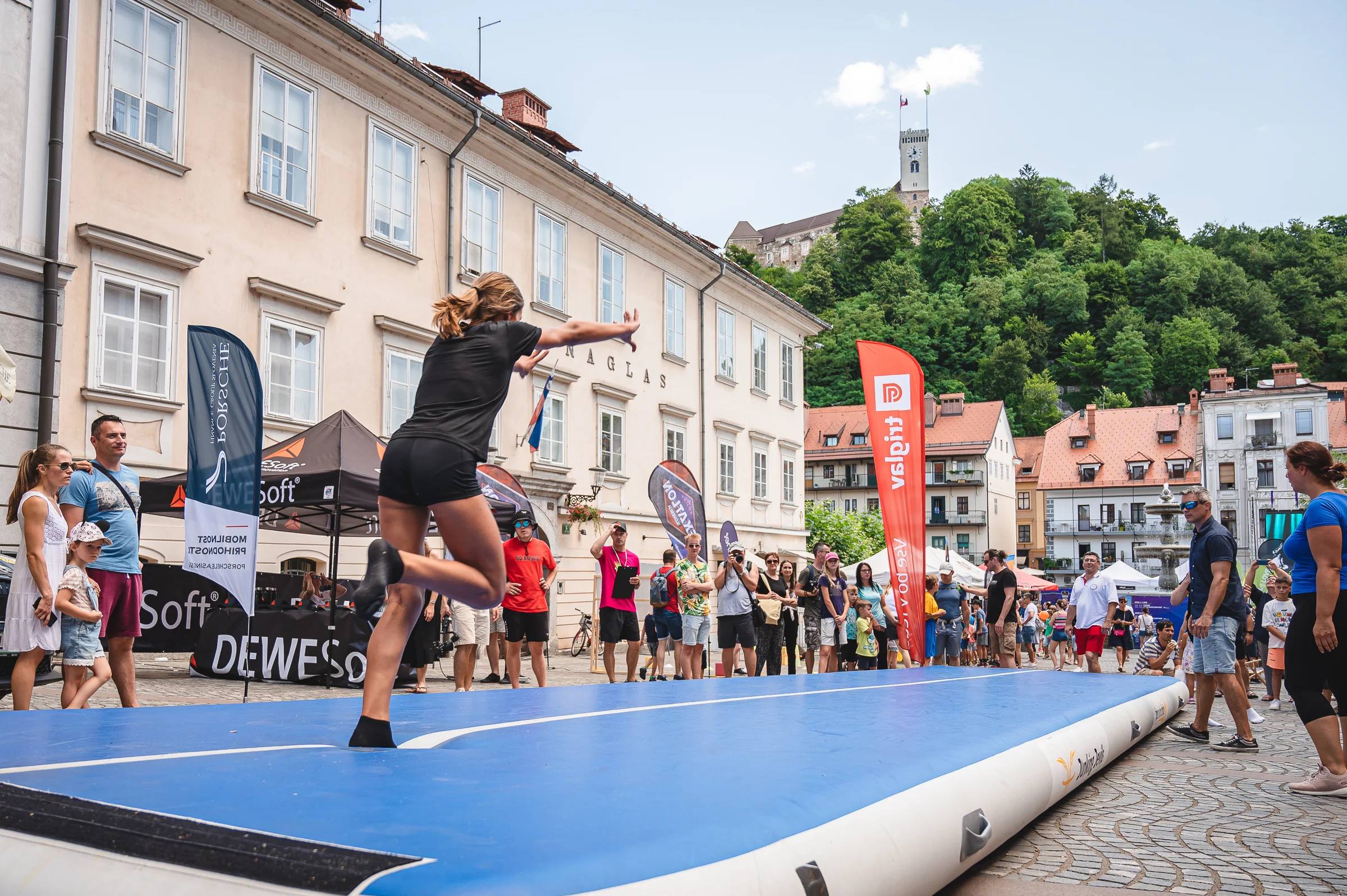 A girl does a cartwheel on an airtrack in a city square while people watch.