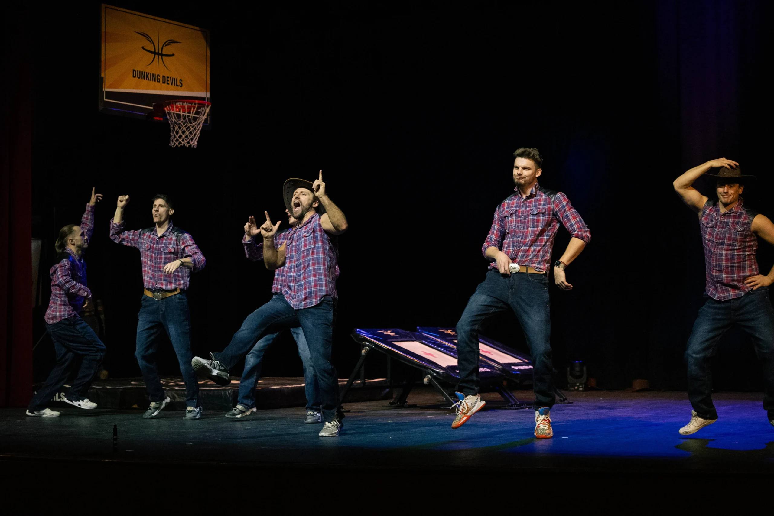 Dunking Devils dancing on stage in checked shirts during an acting scene.