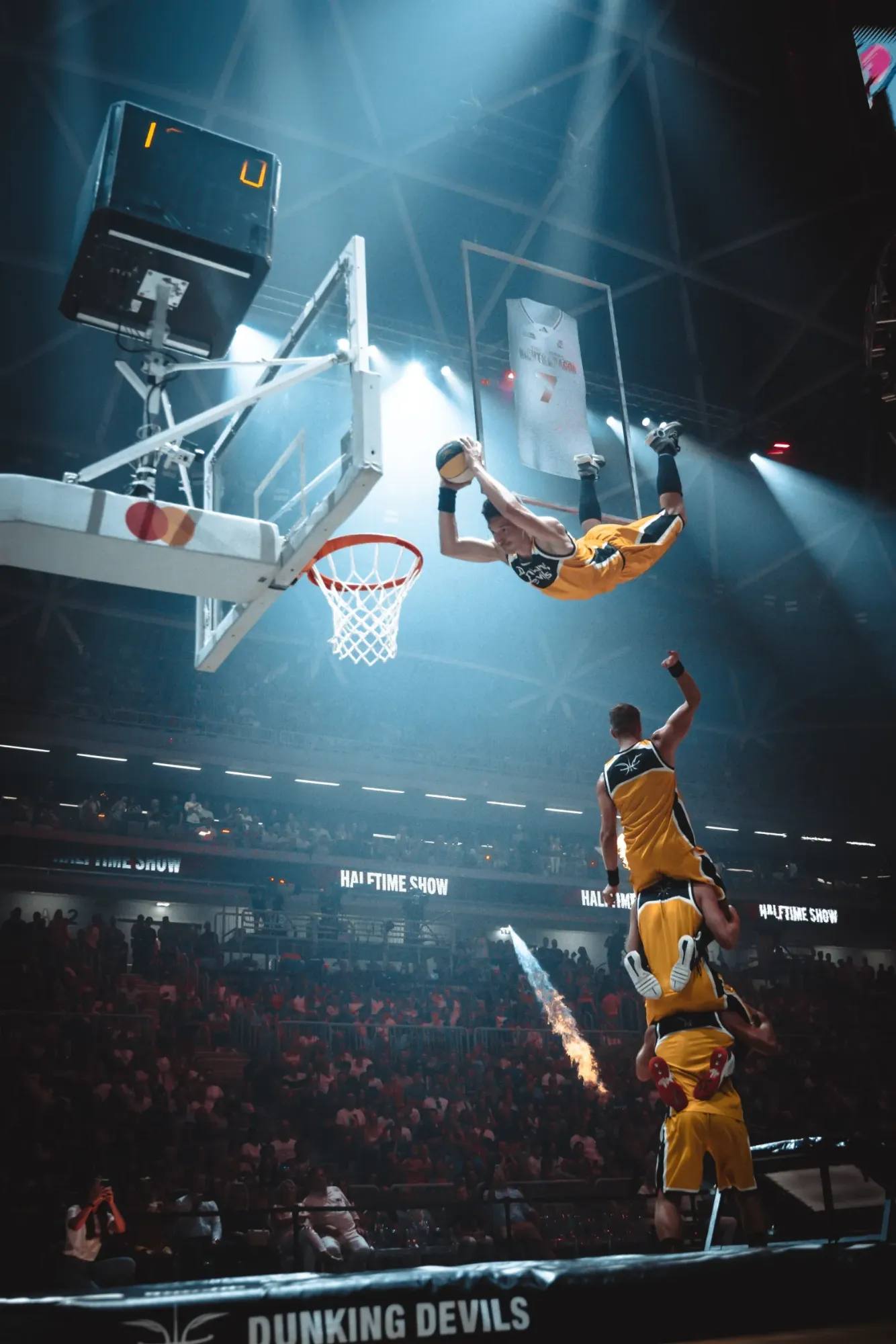 Halbzeitshow der Dunking Devils bei der Night of Dragon: Ein Akrobat fliegt über einen Dreierturm zum Korb, neben dem Spielfeld schießen Flammen in die Höhe.