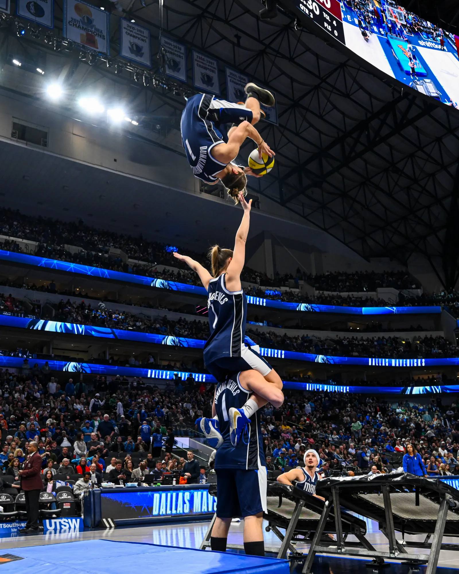 Ein Akrobat der Dunking Devils dreht sich mit dem Ball kopfüber über einem Zweierturm bei einem NBA-Spiel der Dallas Mavericks.