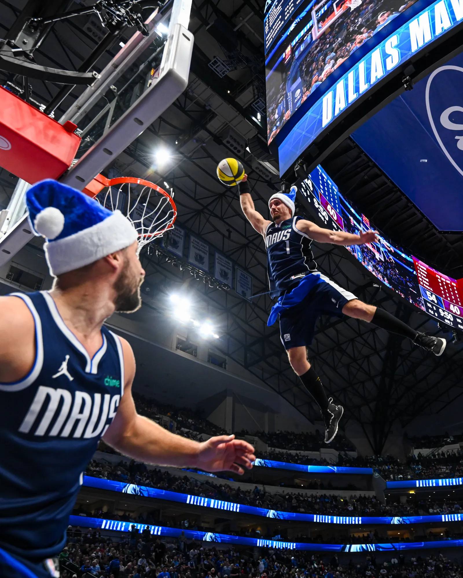 Ein Akrobat der Dunking Devils mit Weihnachtsmütze dunkt unter dem Videowürfel bei einem Feiertagsspiel der Dallas Mavericks.