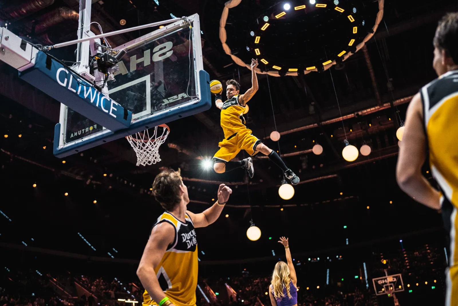 Ein Dunker der Dunking Devils hängt am Ring bei der SHAQ All Stars League in Gliwice, die Teamkollegen schauen vom Spielfeld zu.