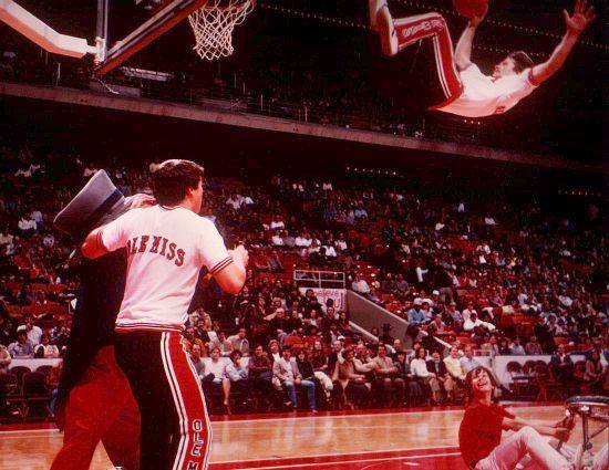 Archival photograph: an Ole Miss performer flips through the air towards the basket during a college basketball game.