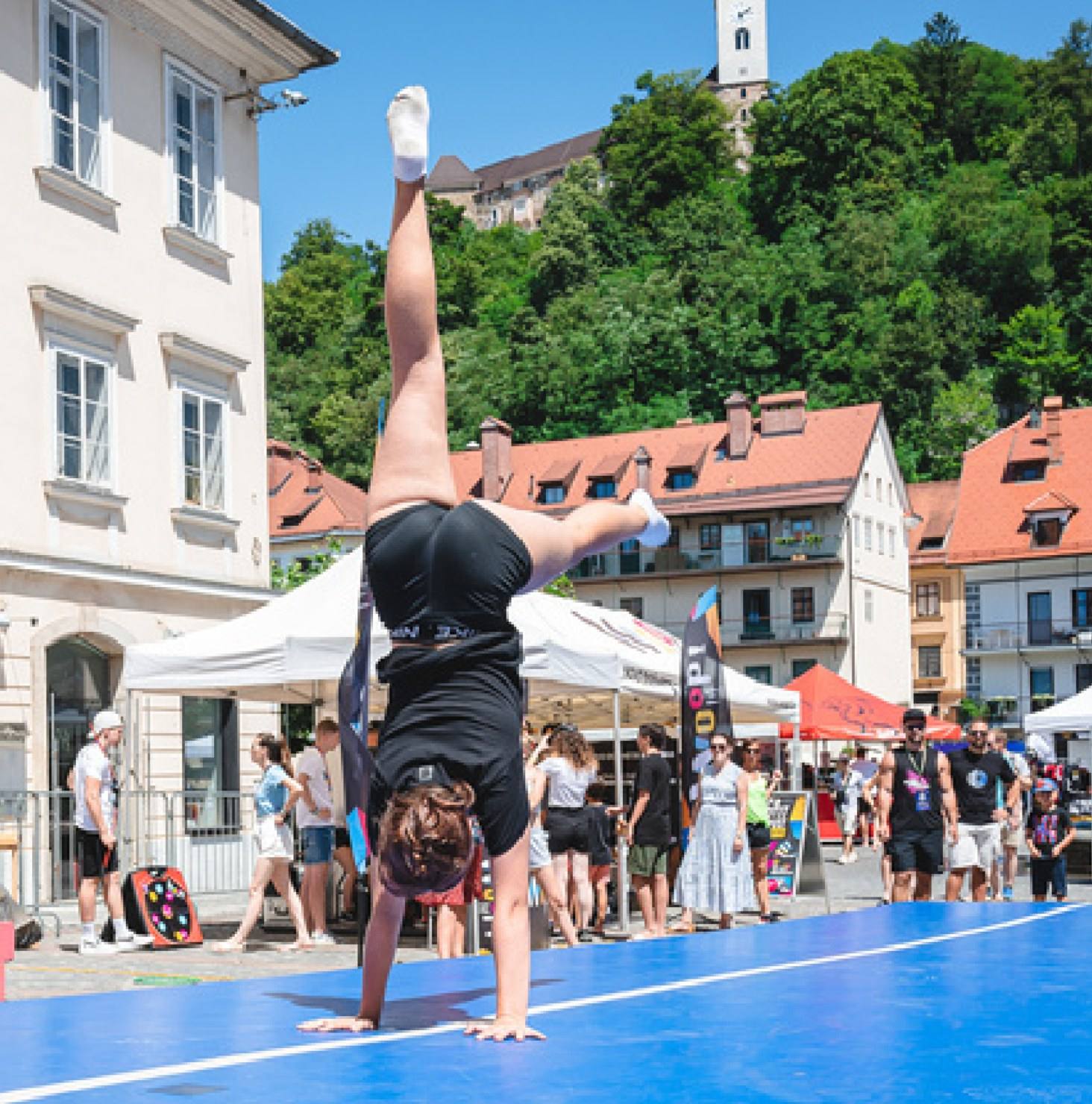 A girl does a handstand on an airtrack in a town square.