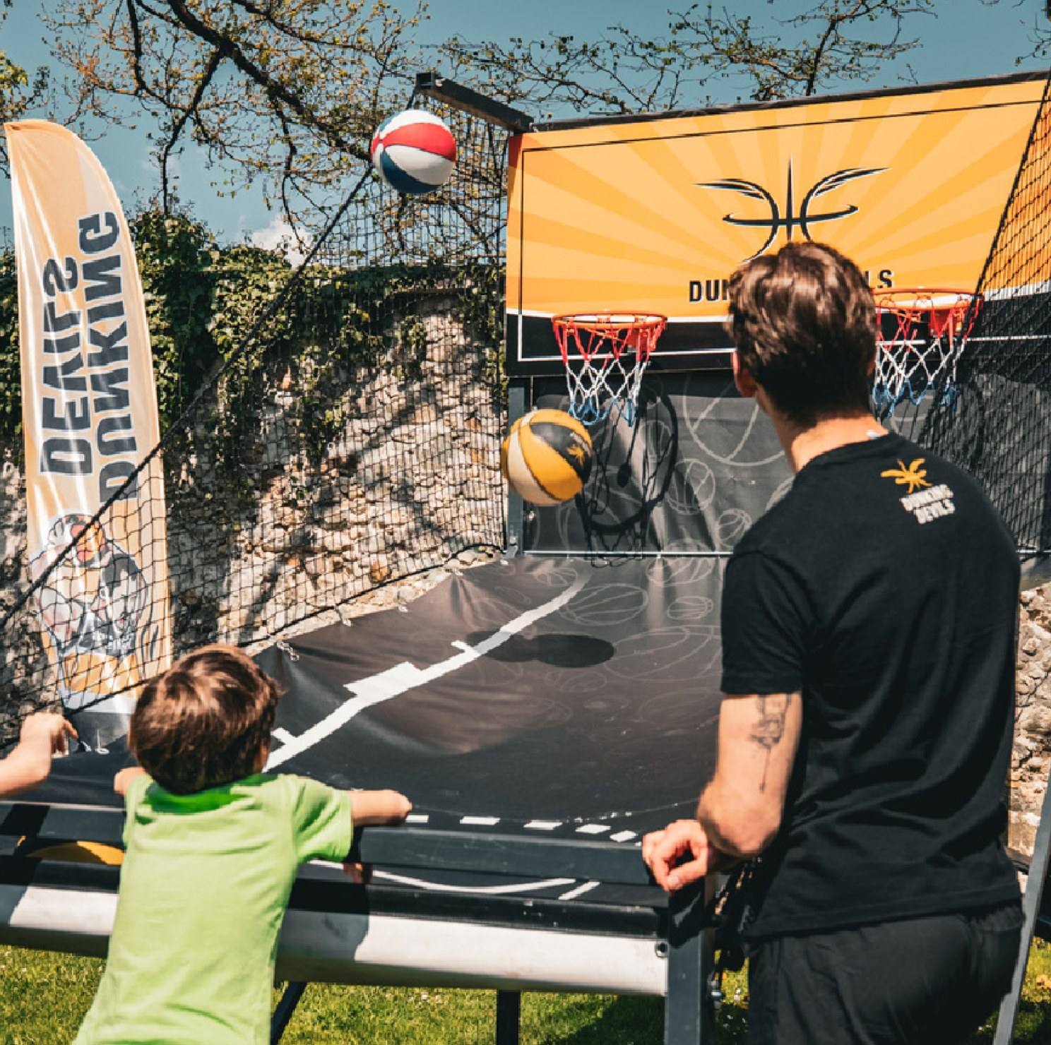 A boy plays a basketball shooting game at a Dunking Devils arcade hoop while a coach watches.