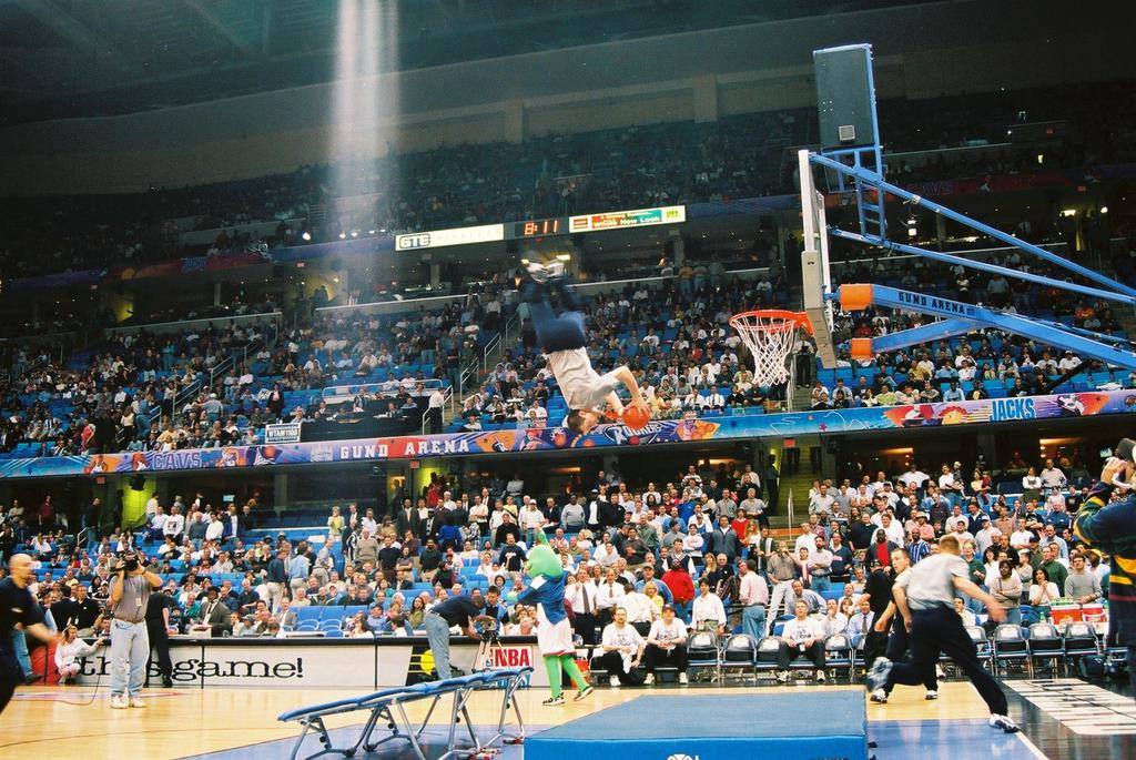 Archival photograph: a Žabe acrobat dunks upside down after a trampoline take-off in a full basketball arena.